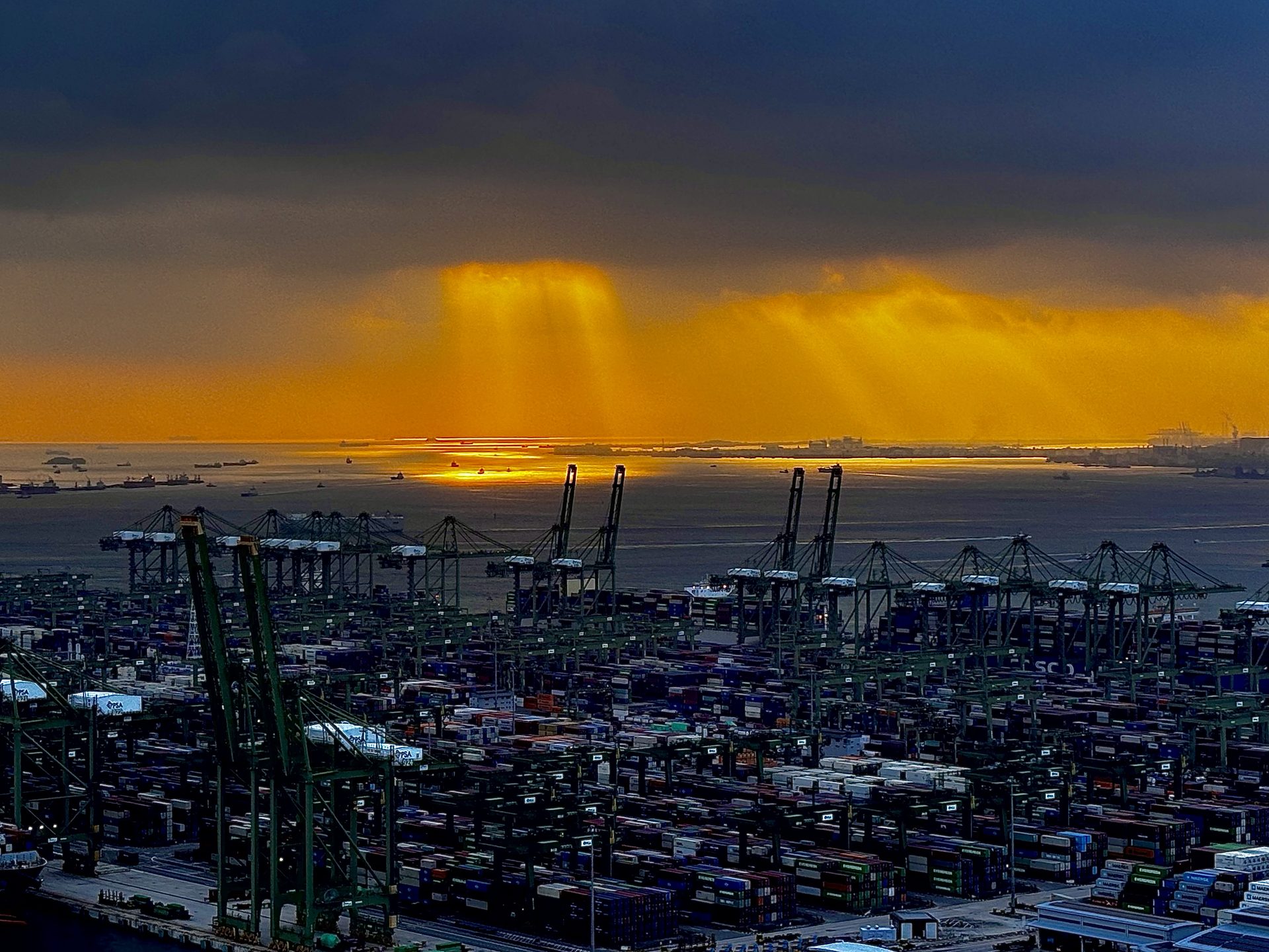 Cranes and stacked containers at Pasir Panjang Container Terminal, Singapore, under a golden evening sky
